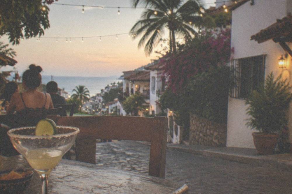 Evening restaurant terrace with string lights above a stone boardwalk in a resort town center