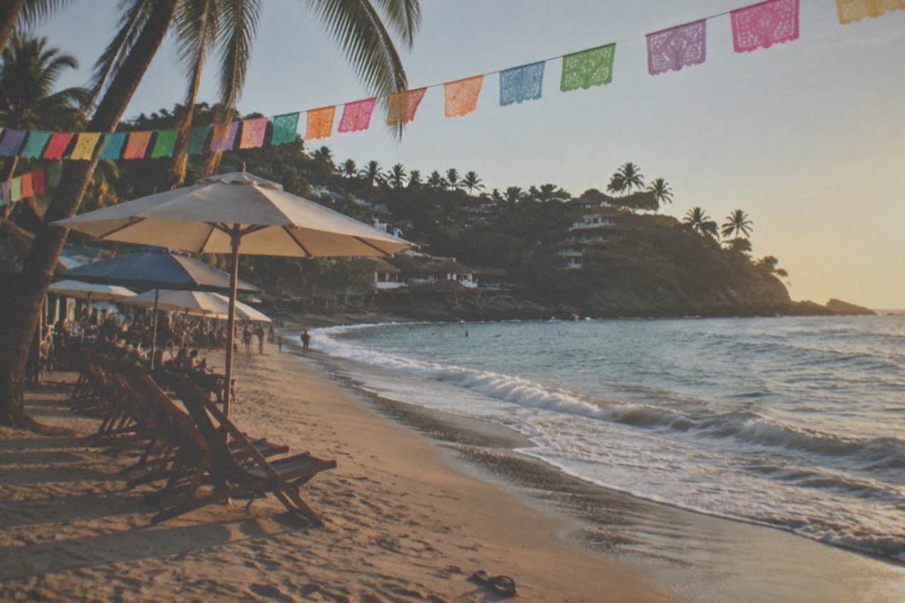 Colorful flags and umbrellas above a sandy beach cove with palm trees and gentle surf