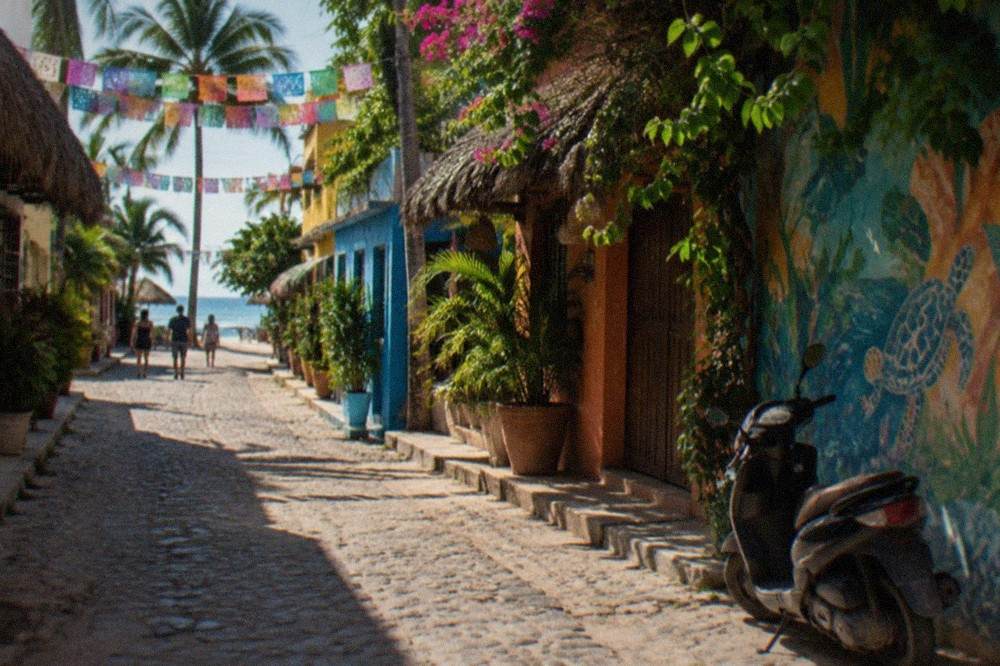 A narrow street of colorful storefronts and hanging paper flags in a beach town