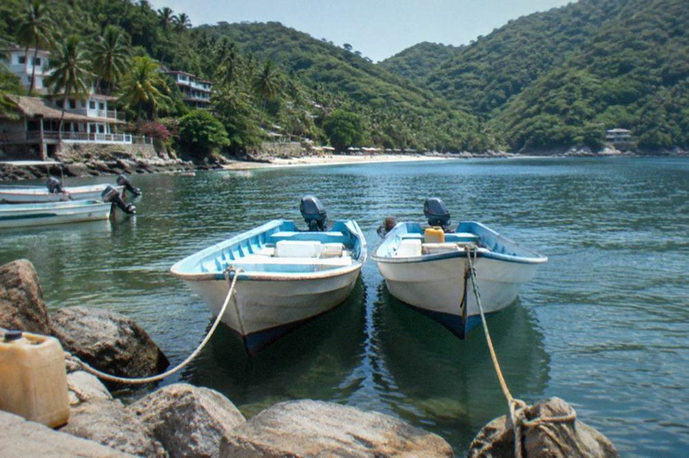 Small open boats moored at a rocky shoreline beside a calm bay in the late morning
