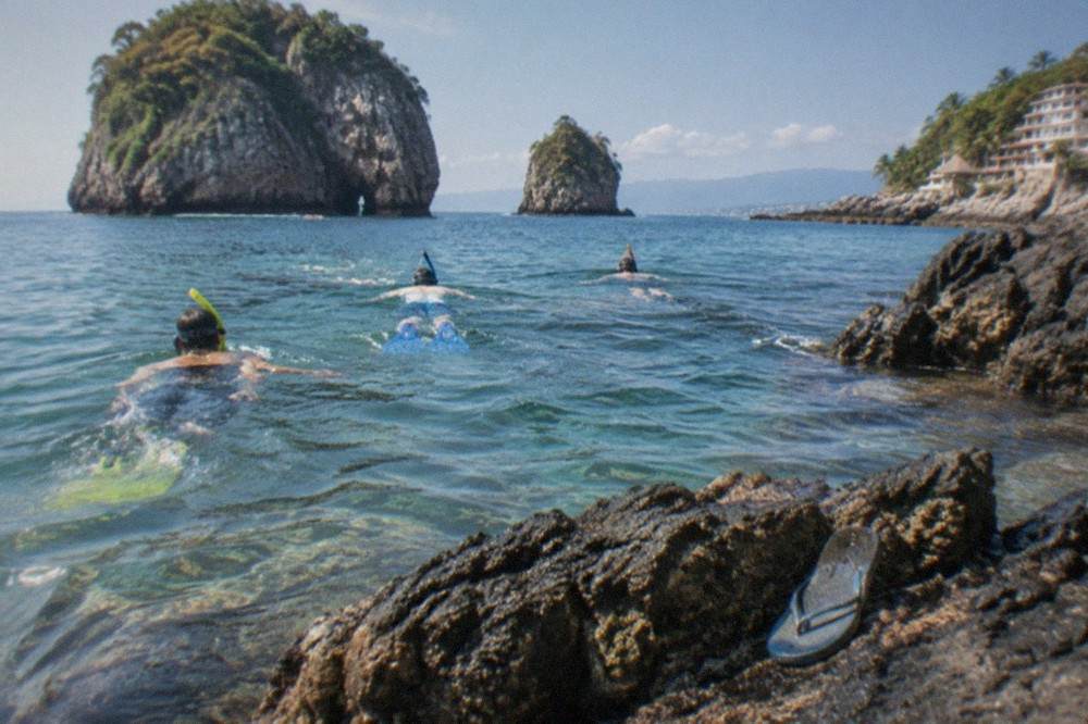 Snorkelers floating over dark volcanic rocks in clear Pacific bay water