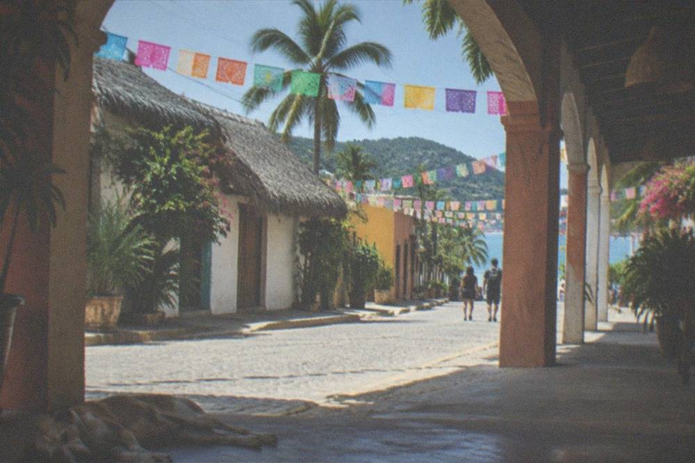 A quiet village street with colorful flags strung between low buildings under blue sky