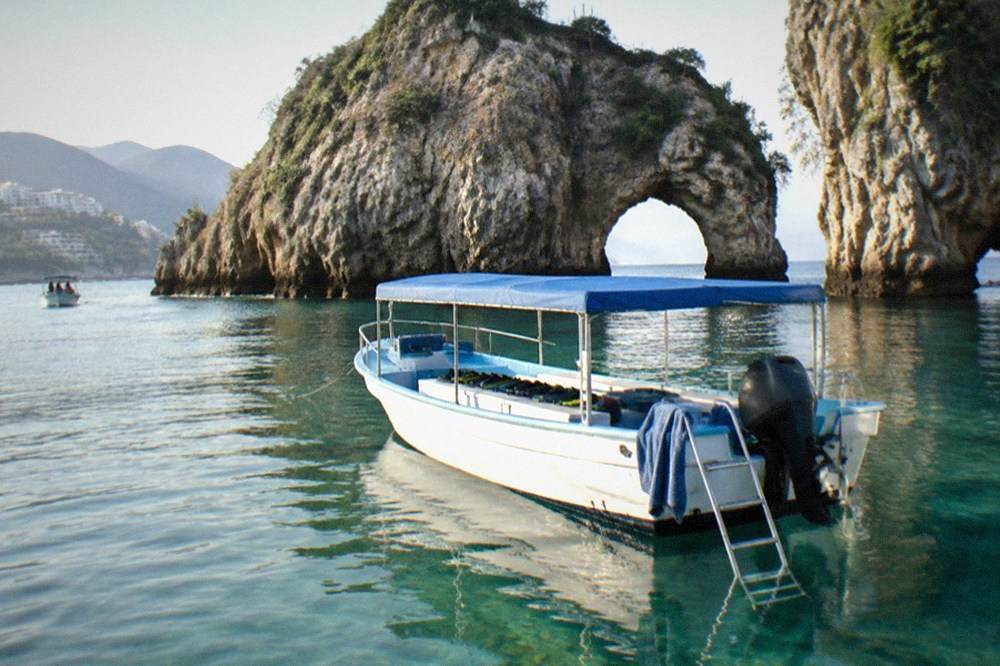 An empty snorkel boat moored in clear water beside a rocky island on a calm morning