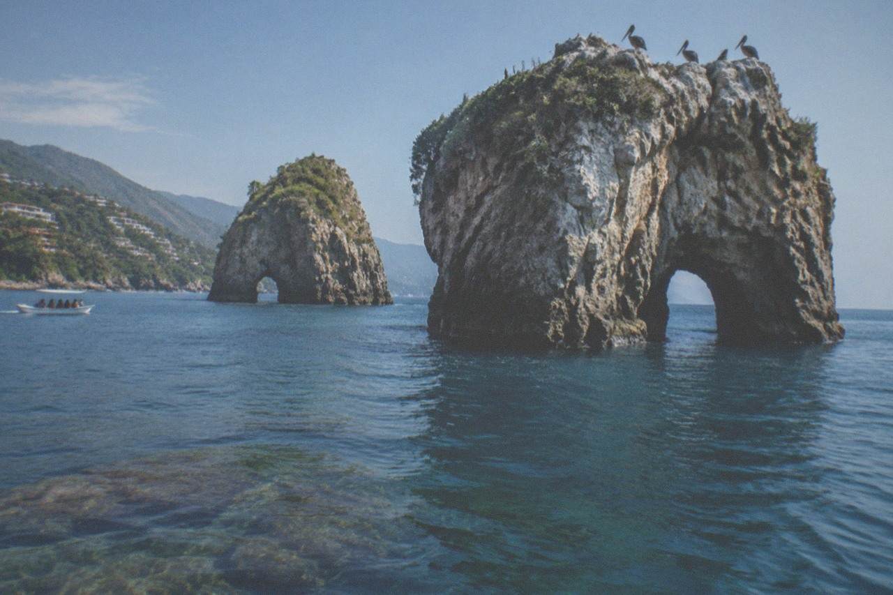 Granite islands of Los Arcos rising from calm blue water with a rocky reef visible beneath the surface