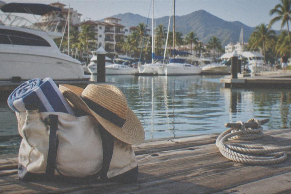 Beach bag with towel, hat and water bottle on a wooden deck