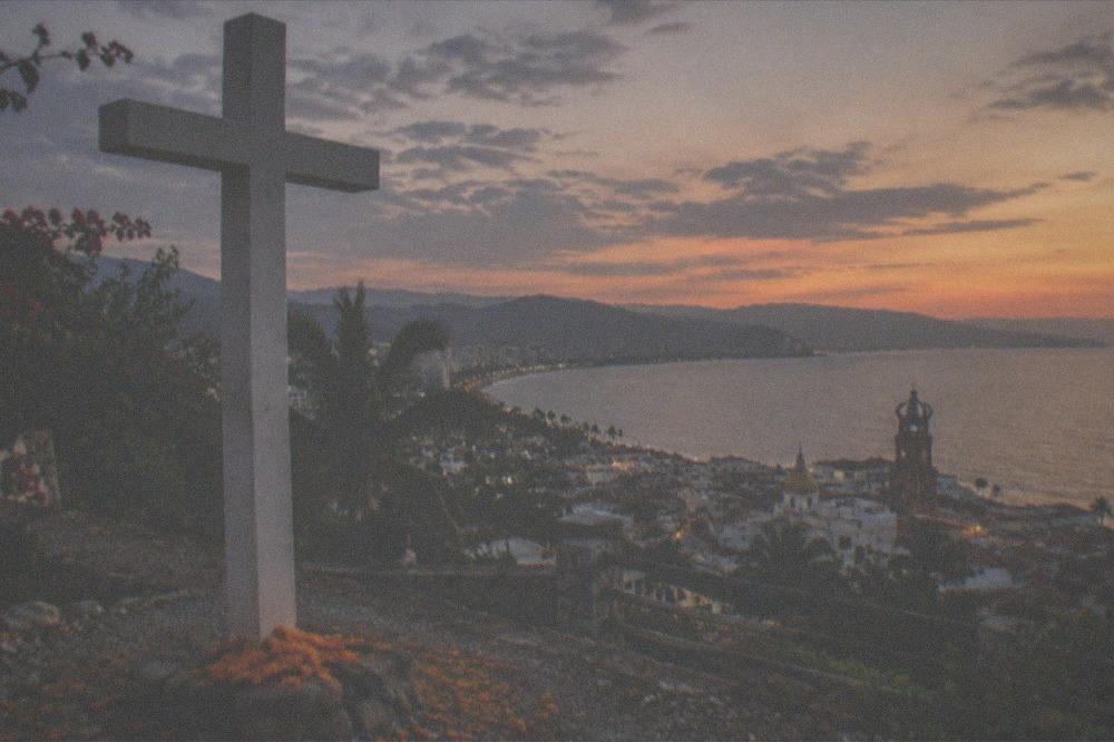 A panoramic view from a hilltop lookout over a bay and city with a large cross in the foreground
