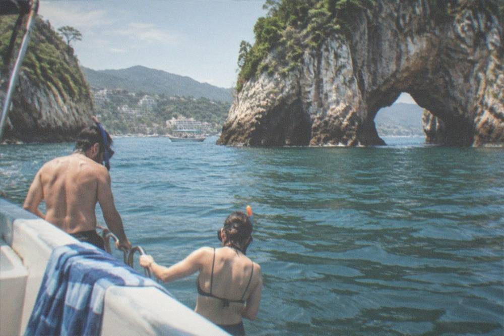 Snorkelers in the water beside a small boat near rocky shoreline