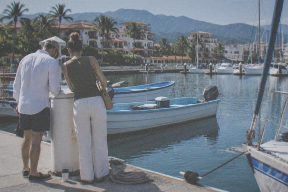 Couple reviewing a map and tablet at a marina dock beside tour boats