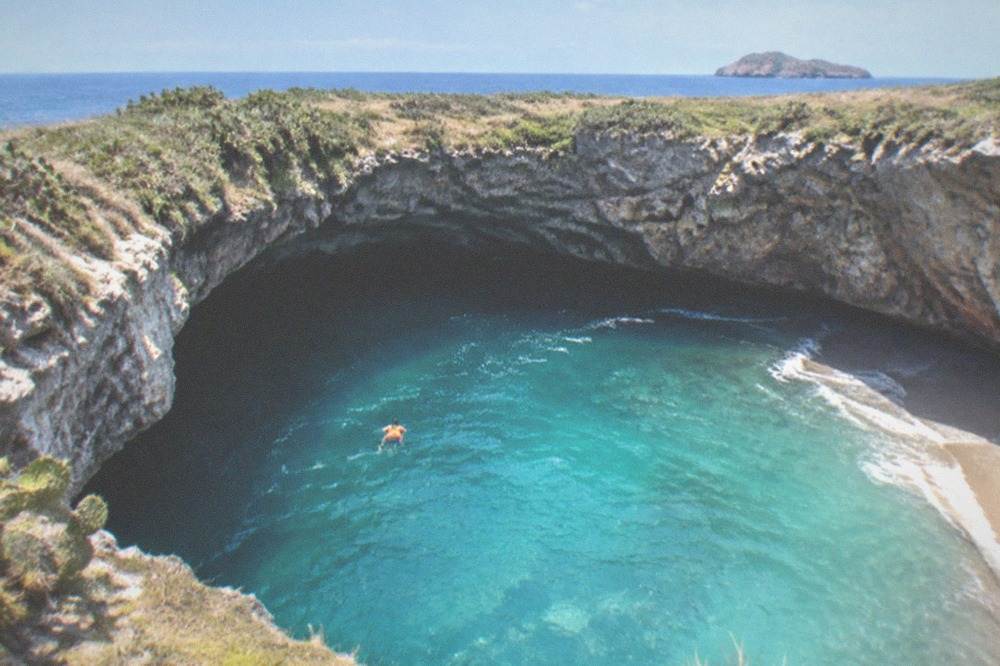 Turquoise water filling a collapsed rock cove surrounded by steep stone walls