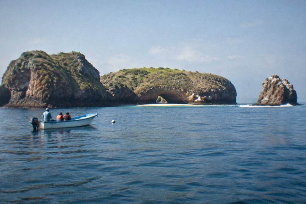Granite islands rising from calm blue ocean with a small boat nearby