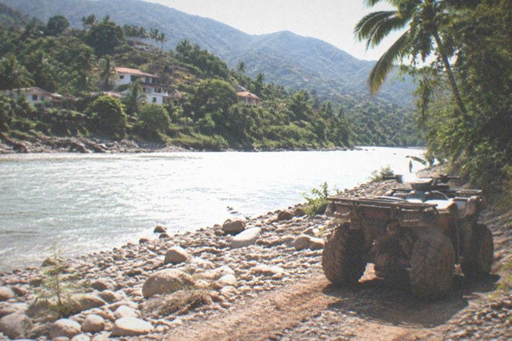 An all-terrain vehicle on a dirt trail beside a jungle river