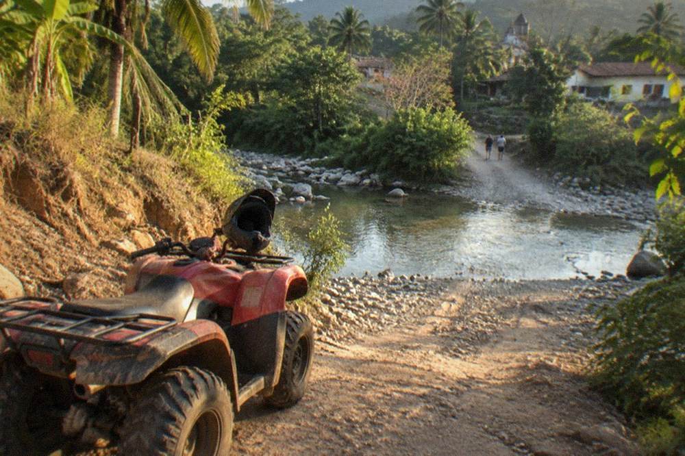 ATV parked on a jungle dirt trail beside a river crossing in the Sierra Madre foothills
