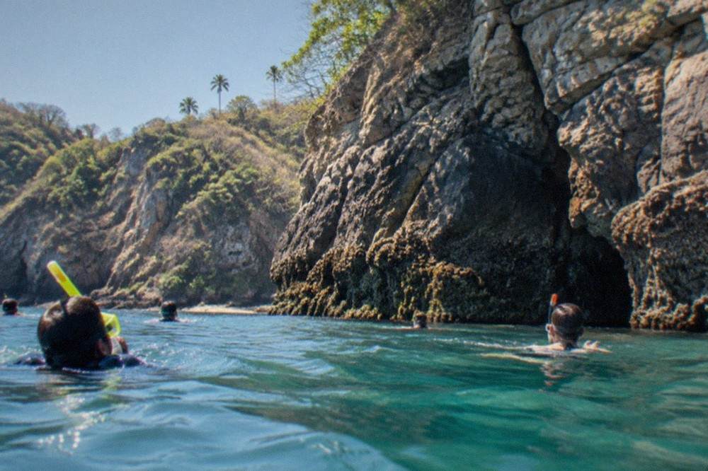 Snorkelers in calm turquoise water beside a rocky island shoreline