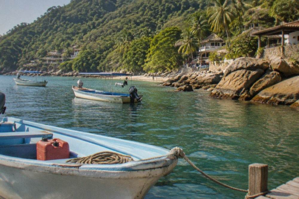 Small open boats moored at a rocky shoreline with jungle hills rising behind them