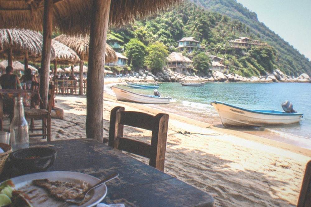 A calm beach cove with thatched-roof restaurants and small boats resting on the sand